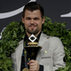 Chess World Champion Magnus Carlsen holds a trophy and smiles.